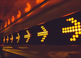 A series of glowing arrow signs in a city environment, indicating direction at night.